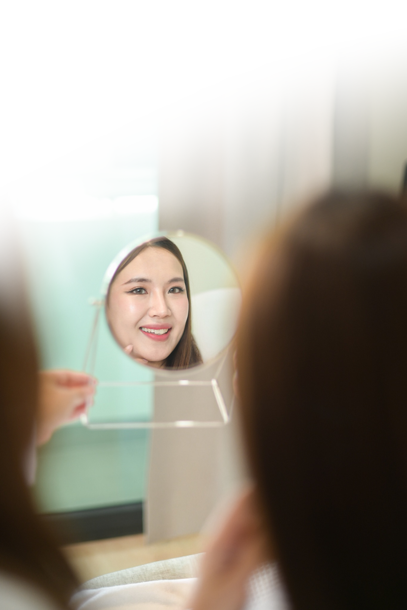 Asian woman inspecting her reflection in a small mirror